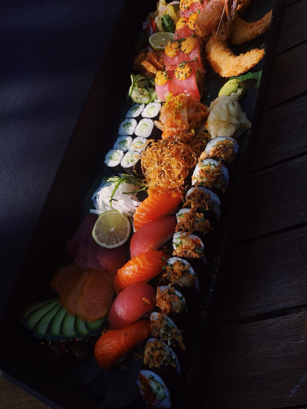Lange Platte mit Nigiri, Sashimi, Rolls und Tempura-Garnelen auf dunklem Holz