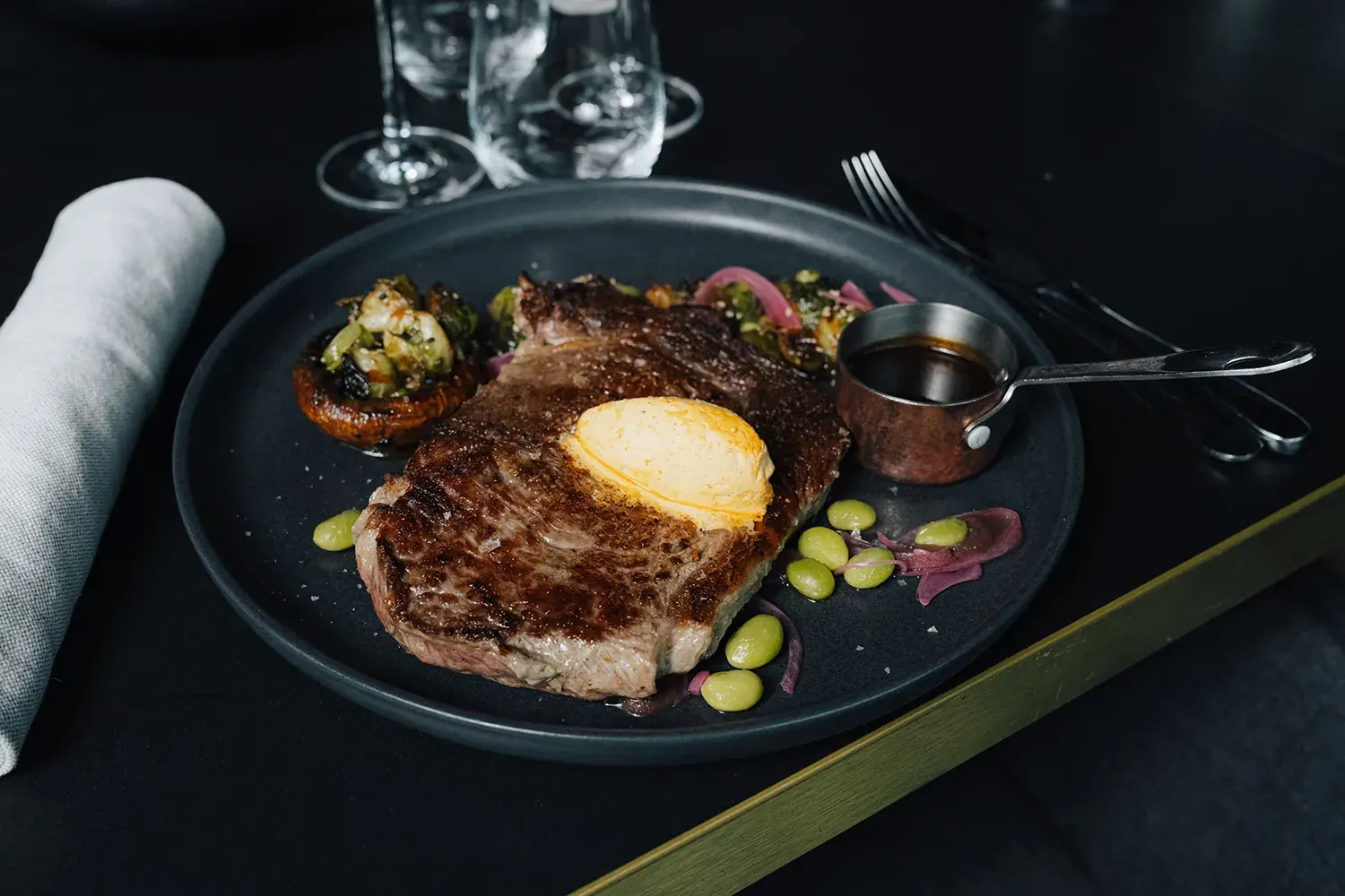 Dry-Aged-Steak mit Jus, Ei und Gemüse auf dunklem Teller
