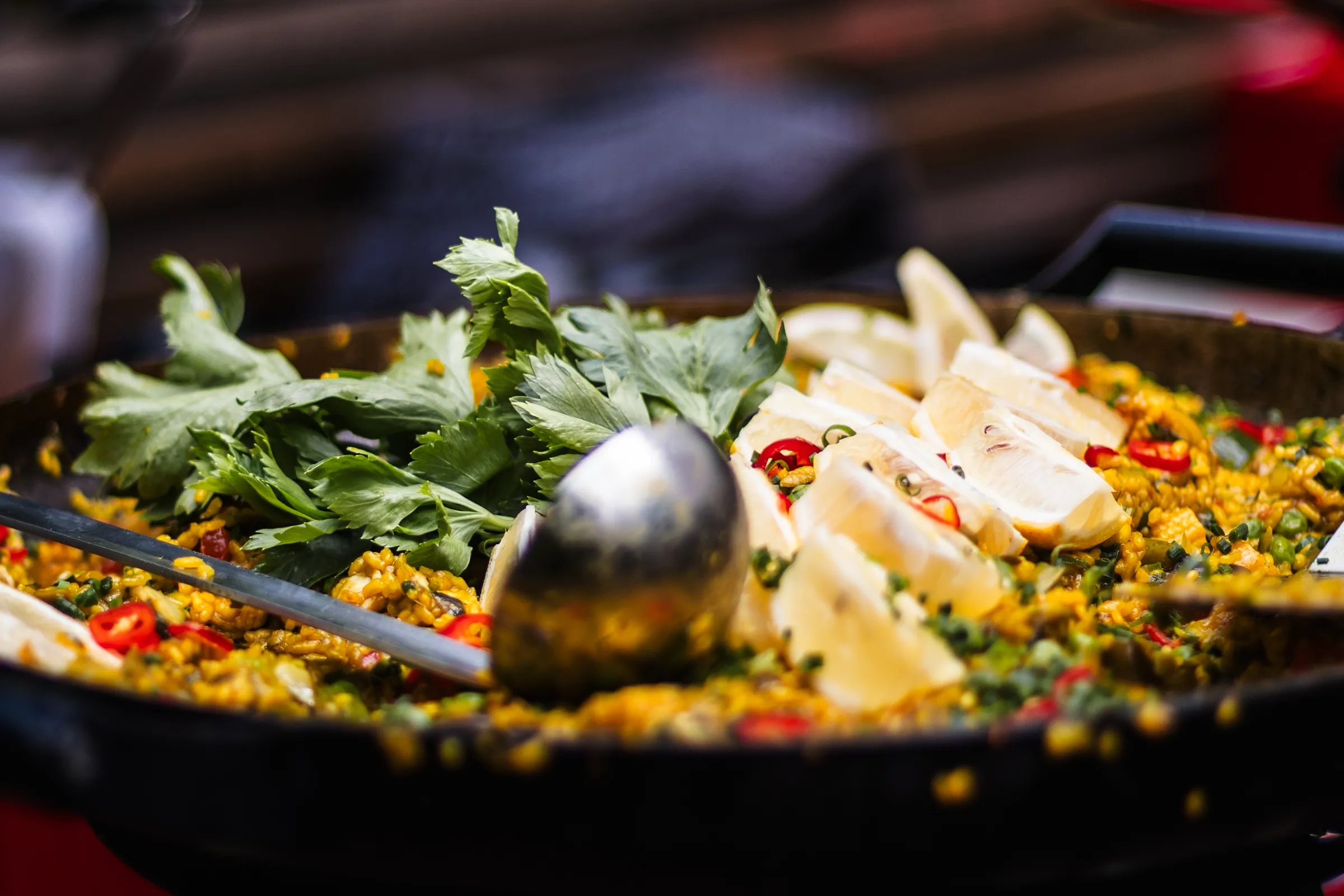 Große Paella-Pfanne mit Safranreis, Zitronen, Chili und frischen Kräutern beim Live-Cooking