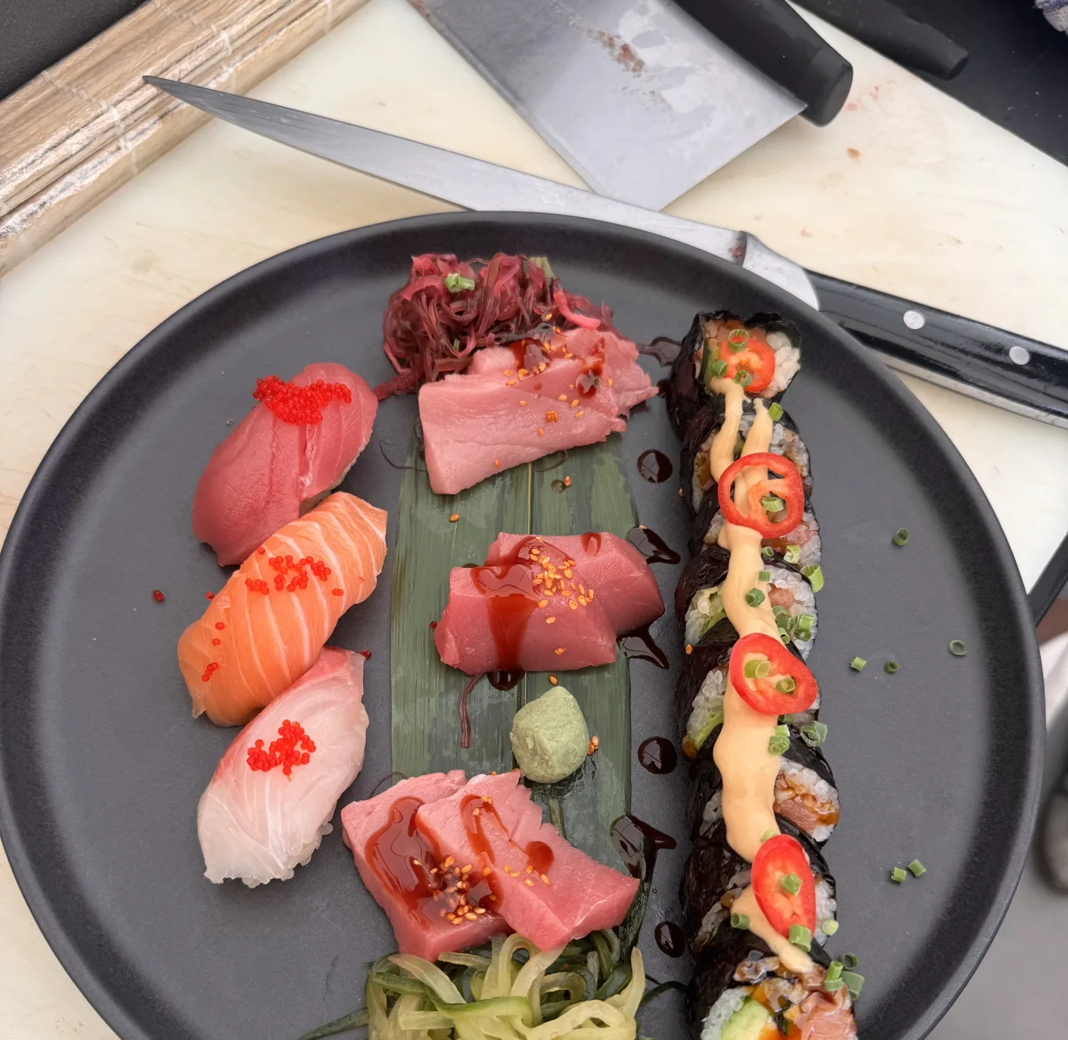 Teller mit Nigiri, Sashimi und einer langen Rolle, direkt am Counter angerichtet